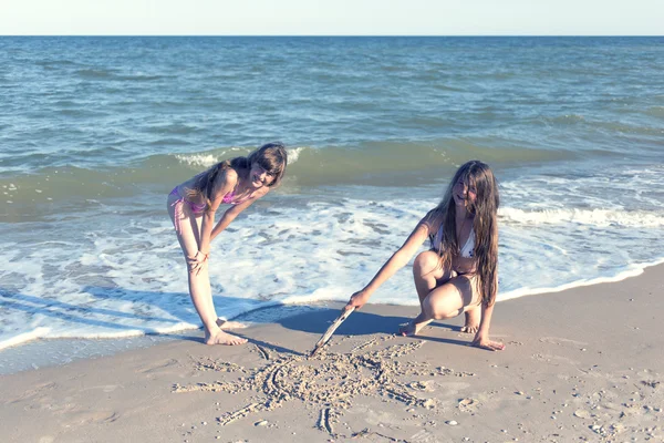 Girls drawing in the sand on the beach in the summer sun. — Stock Photo, Image