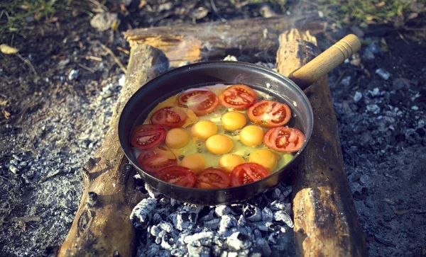 Cooking breakfast  over a campfire at a campsite.
