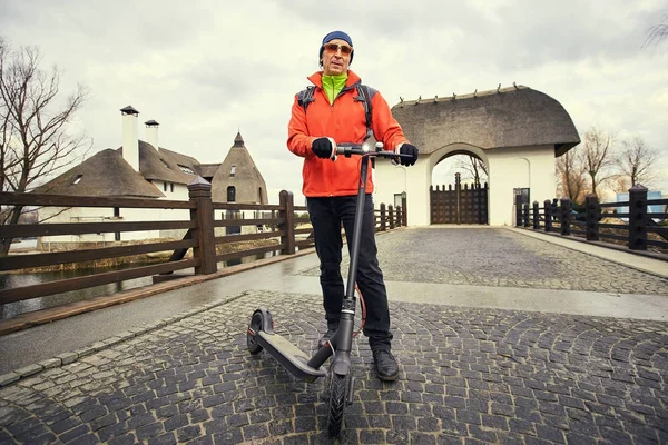 Een man in een rood jasje met een rugzak en een scooter op de stree — Stockfoto