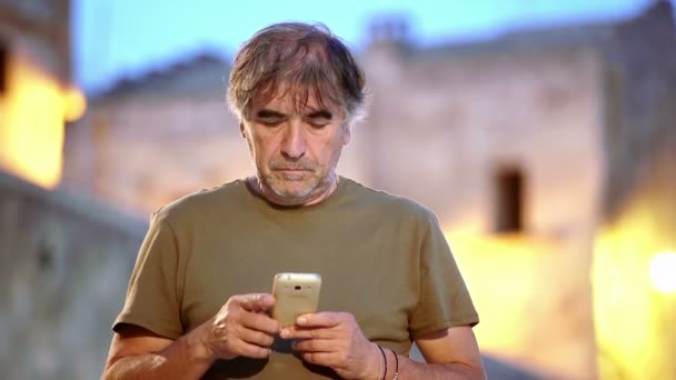 50 year old man writes a message with his smartphone in the ancient city — ストック動画