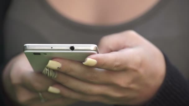 Mujer joven con esmalte de uñas amarillo escribiendo en el móvil — Vídeos de Stock