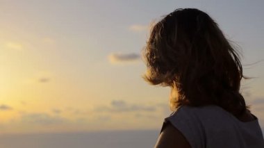 Rüzgar saç hareket ederken batımında denize bakan yalnız genç kadın