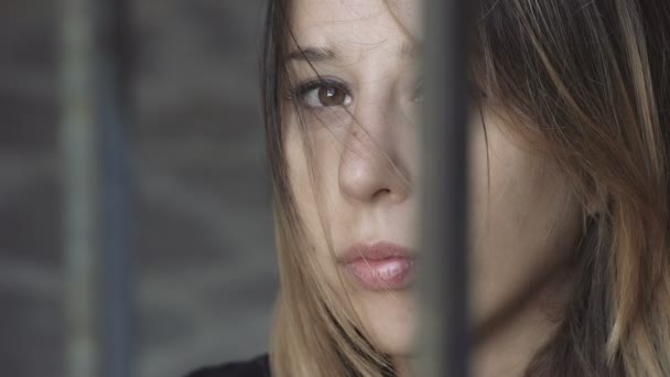 Sad and melancholy girl behind bars, stares camera — Stock video