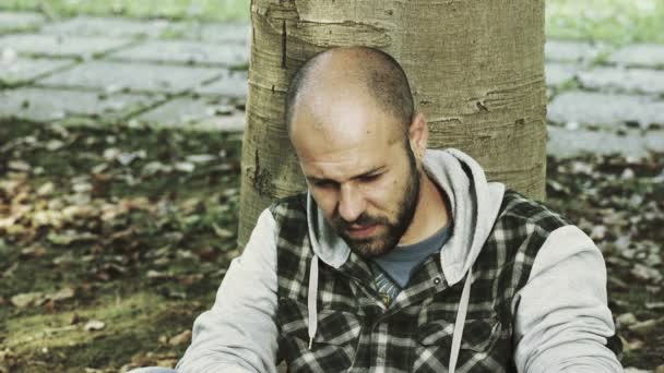 Joven drogadicto apoyado en un árbol mirando hacia arriba — Vídeos de Stock