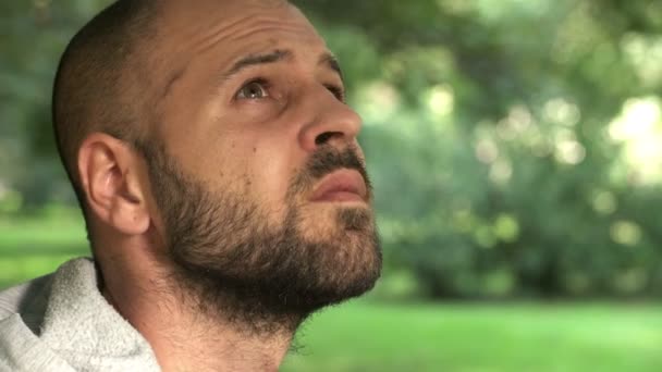 Bald man alone in the park looks up at the sky to see if it would start to rain — Stock video