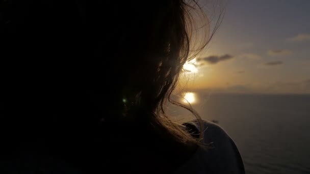 Joven mujer de vuelta en retroiluminación contempla la puesta de sol — Vídeos de Stock