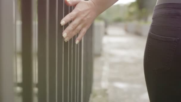 Silhouette of woman walking by touching the bars of a gate — Stock Video