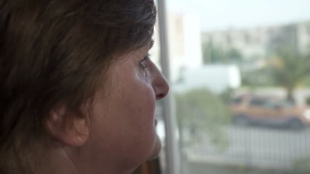 Пожилая женщина задумчиво смотрит в окно — стоковое видео