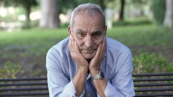 Sad retiree on a park bench looking at the camera sadly — Αρχείο Βίντεο