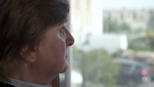 Пожилая женщина одна смотрит в окно — стоковое видео