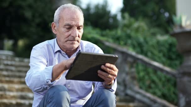 Oude man zit op de trappen de tablet gebruiken — Stockvideo