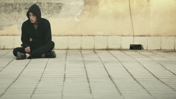 Jeune SDF assis sur le sol fumant une cigarette — Video