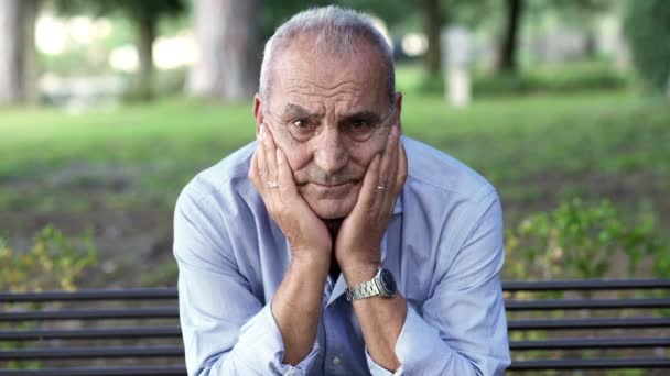 Sad old man on a park bench looking at the camera sadly — Αρχείο Βίντεο