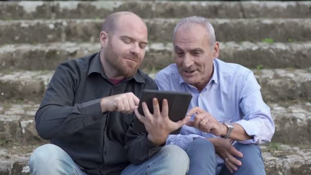 Vater und Sohn sitzen draußen und schauen dem Tablet zu — Stockvideo