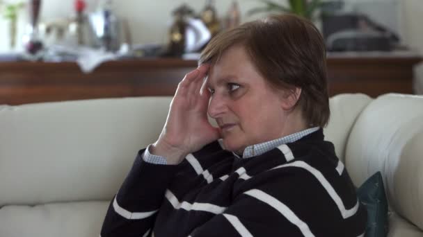 Elderly woman with a  headheache sitting on white sofa — Stock video