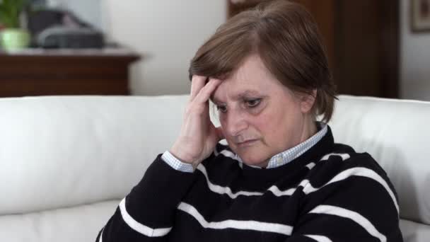 Зрелая женщина сидит на диване с сильной головной болью — стоковое видео