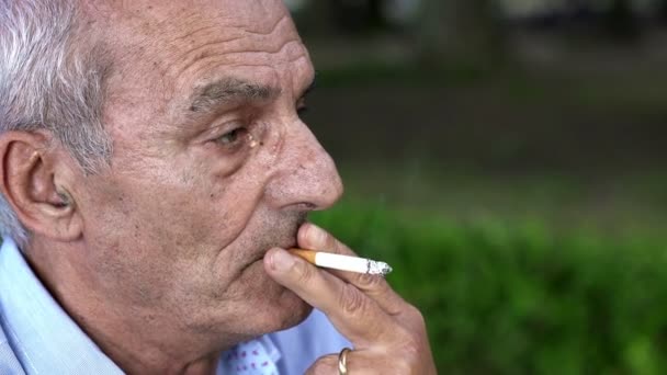 Un hombre mayor pensativo fuma un cigarrillo en el parque — Vídeo de stock