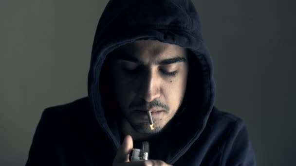 Mladý muž s kapucí rozsvítí cigaretu vyzývavě — Stock video