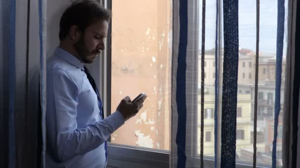 Привлекательный бизнесмен у окна пользуется телефоном — стоковое видео