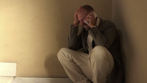 Człowiek w kucki na podłodze nerwowo rozmawia przez telefon — Wideo stockowe
