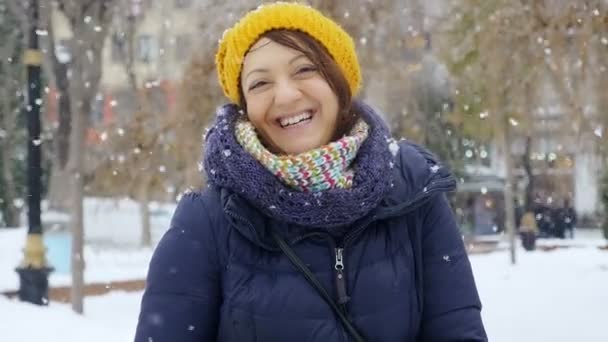 Donna felice sorridente alla macchina fotografica durante una nevicata — Video Stock