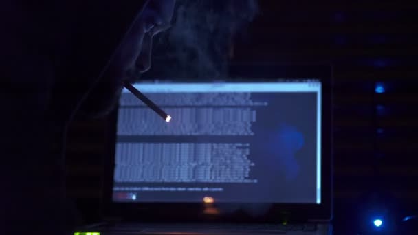 Joven hacker enciende un cigarrillo delante de la computadora — Vídeo de stock