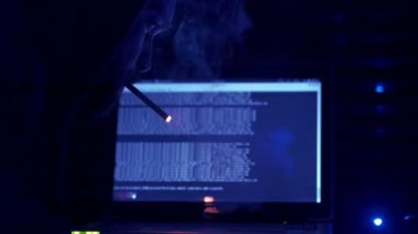 kapüşonlu genç hacker bir bilgisayar ihlal edilmesi sırasında bir sigara yakıyor