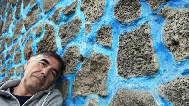 Mature man leaning against a wall with blue stones — Stock Video