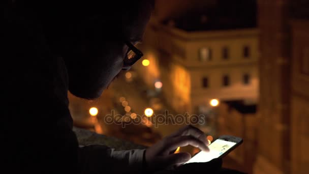 Mann mit Brille in der Dämmerung auf der Terrasse mit seinem Smartphone — Stockvideo