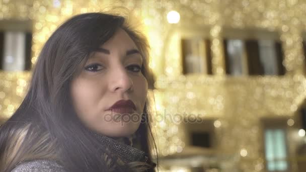 Seriózní žena intenzivně při pohledu na fotoaparát s vánoční osvětlení za — Stock video