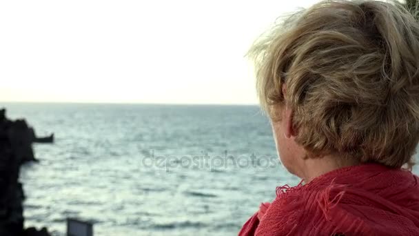 Blonde Frau blickt an einem windigen Tag aufs Meer — Stockvideo