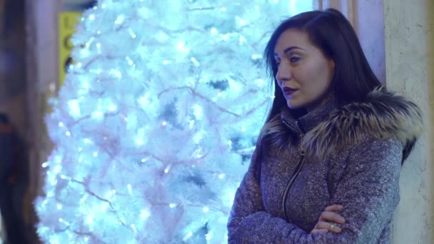 Mujer bastante aburrida cerca de un árbol de Navidad iluminado — Vídeos de Stock