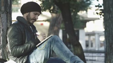 not defterinde yazmak için bir ağaç niyet altında oturan genç adam