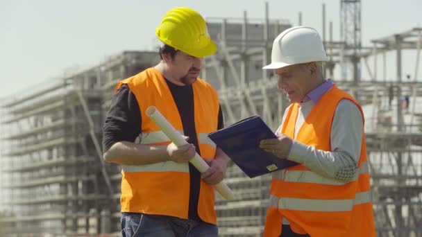 Discusión entre un arquitecto senior y un trabajador en el sitio de construcción — Vídeos de Stock