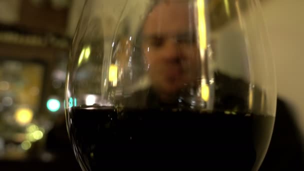 Visão turva através de vidro de vinho tinto de um homem solitário no bar — Vídeo de Stock