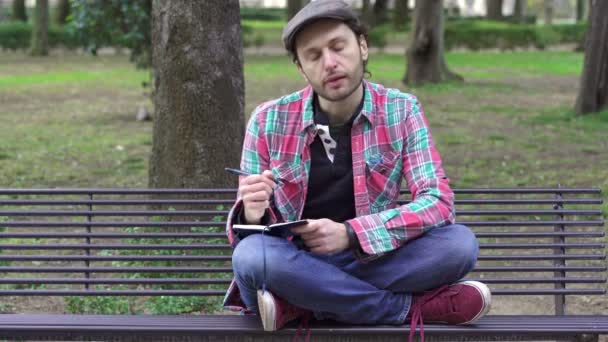 Hombre deprimido en un banco en el parque escribe sus pensamientos en un diario — Vídeos de Stock