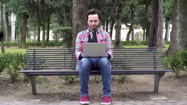 Junger Schriftsteller schreibt auf seinem Laptop im Park — Stockvideo