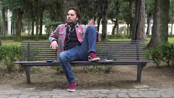Расслабленный случайный человек на скамейке слушает музыку время ведения — стоковое видео