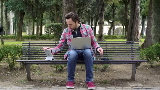 Журналист в парке с помощью планшетов, смартфонов и ноутбуков — стоковое видео