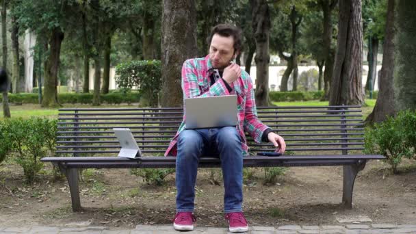 Jóvenes autónomos trabajan en el parque con ordenadores portátiles, tabletas y smartphones — Vídeo de stock