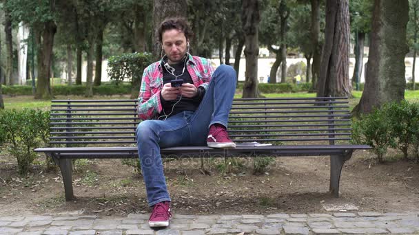 Uomo casual in panchina ad ascoltare musica con il suo smartphone — Video Stock