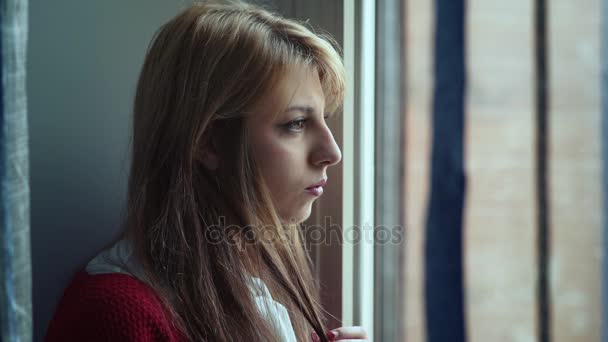 Mujer rubia triste en la ventana tocando el cabello nerviosamente — Vídeos de Stock