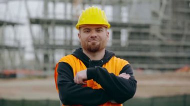 Ciddi inşaat işçisi kollarını aşar ve kameraya bakıyor