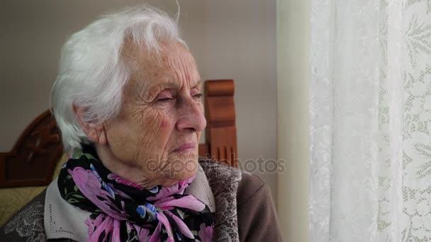 Παλιά, λυπημένη γυναίκα μοιάζει pensively έξω από το παράθυρο — Αρχείο Βίντεο