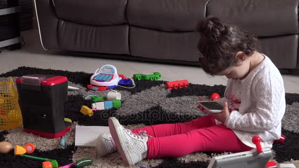 Dulce niña sentada en el suelo jugando con el teléfono inteligente — Vídeos de Stock