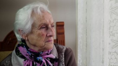 dalgın ve sıkılmış yaşlı kadın pencereden görünüyor