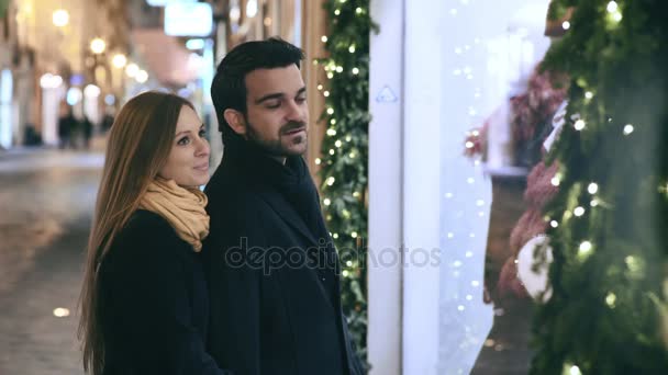 Jovem casal observa uma janela de uma loja conversando — Vídeo de Stock