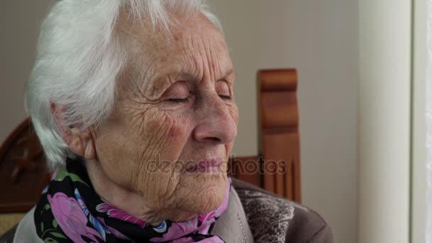 Verdrietig en nadenkend oude vrouw zitten in de buurt van het venster — Stockvideo