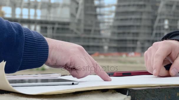 Ręce inżynierów, które wskazują projektu na placu budowy — Wideo stockowe