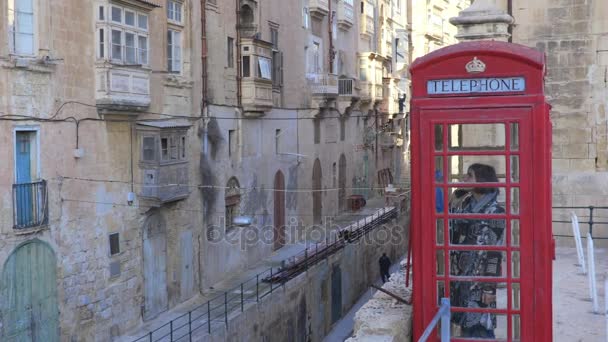 Valletta, Malta-žena mluví o telefonu v červené telefonní budky v malé vesnici — Stock video
